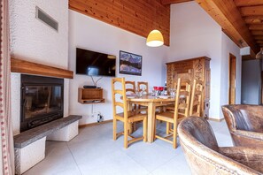 A cozy living room with a fireplace, wooden dining table, and chairs. - 3-bedroom apartment in Veysonnaz (Veysonnaz)