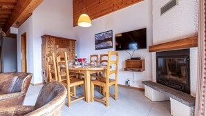 Un coin repas chaleureux, avec des meubles en bois, une cheminée et un téléviseur fixé au mur.