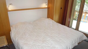 Ein Schlafzimmer mit einem großen Bett, einem Holzkopfteil, zwei Nachttischlampen und Blick ins Freie durch eine Schiebetür.