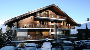 Ein mehrstöckiges Holzchalet mit Balkonen, einer Seilbahn und einem Parkplatz mit Autos.