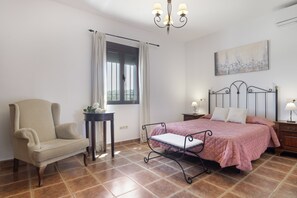 A bedroom with a bed, a chair, a nightstand, a lamp, a window with curtains, and a painting on the wall.