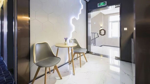 A modern lobby with a hexagonal light feature on the wall, two round tables with chairs, and a clear view of the staircase in the background. - yibaijiudianlangaoluditiezhandian (Shanghai)