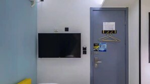 A hotel room with a bed, a flat-screen TV mounted on the wall, a door with a hanger, and a small table with a phone and a card. - yibaijiudianlangaoluditiezhandian (Shanghai)
