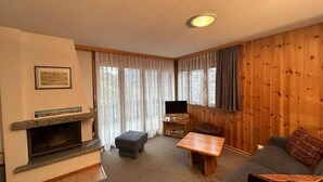 A living room with a fireplace, a television, a sofa, and a wooden wall.