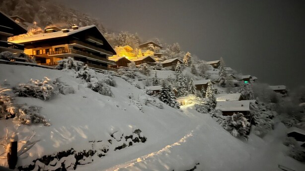 A snow-covered mountain village with illuminated buildings and a prominent hotel with multiple floors and balconies.