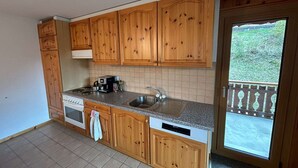 A kitchen with wooden cabinets, a built-in oven, a dishwasher, and a window overlooking a balcony.
