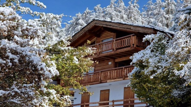 Een houten chalet met een balkon, omringd door sneeuwbedekte bomen.