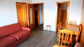 Een knus woongedeelte met een rode bank, een houten eettafel met stoelen en een klein krukje.
