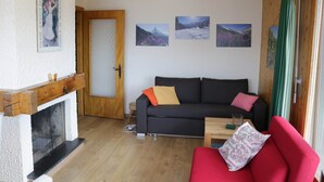 Un salon chaleureux avec une cheminée, un canapé, un fauteuil rouge et trois tableaux encadrés accrochés au mur.