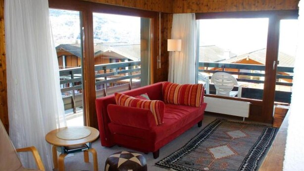 A cozy room with a red sofa, a small round table, and a patterned rug. - Apartment in Veysonnaz with Mountain Views (Veysonnaz)