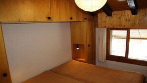 A room with a bed, wooden walls, a window with curtains, and a hanging light fixture. - Apartment in Veysonnaz with Mountain Views (Veysonnaz)