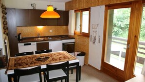 A kitchen with a dining table, chairs, a hanging light fixture, and a window with curtains. - Apartment in Veysonnaz with Mountain Views (Veysonnaz)