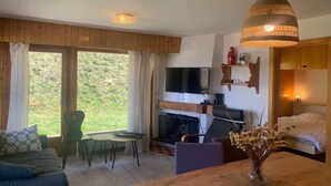 A cozy room with a sofa, a dining table, a TV, a fireplace, and a large window offering a view of the outdoors. - Apartment in Veysonnaz near Ski area (Veysonnaz)