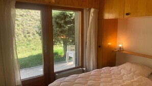 A bedroom with a bed, a window with curtains, a view of a garden, and a wall-mounted light. - Apartment in Veysonnaz near Ski area (Veysonnaz)