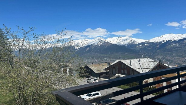 A mountain view with snow-capped peaks, a clear blue sky, and a residential area with houses and parked cars. - Apartment in Veysonnaz near Ski area (Veysonnaz)