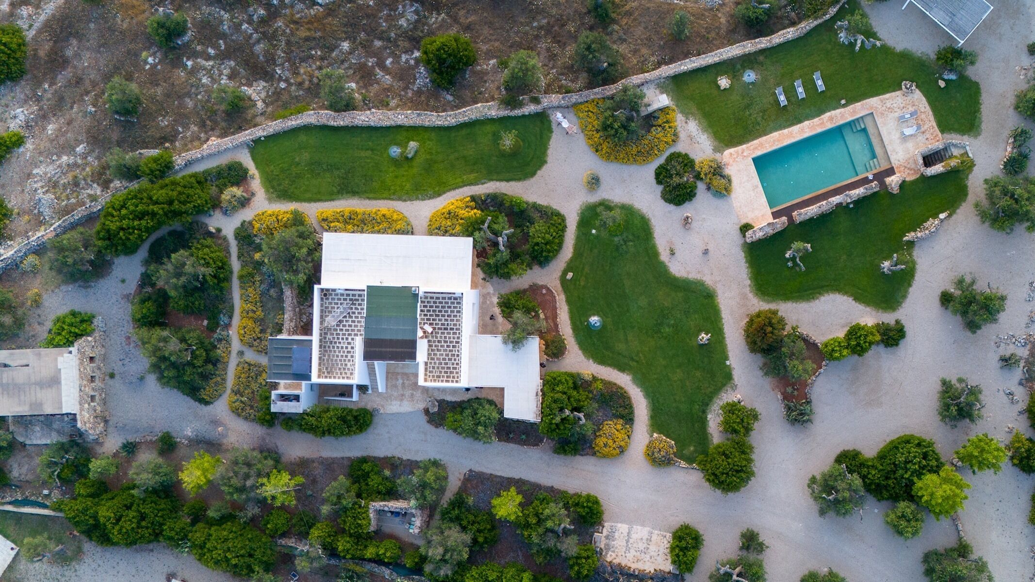 Vue aérienne d’une propriété comprenant une piscine, un grand bâtiment à plusieurs sections et des jardins aménagés.