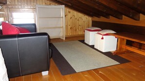 Een gezellig slaapkamer onder het dak met houten plafond, een zwarte leren bank, een klein wit bed en een houten bankje.