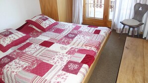 Een bed met een quilt in rood en wit, een houten hoofdbord en een stoel bij het raam.