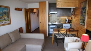 Ein kompakter Wohnraum mit Sofa, Esstisch und Stühlen, Küchenzeile mit Herd und Backofen sowie Holzboden.