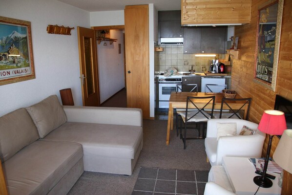 A compact living space with a sofa, a dining table with chairs, a kitchen area with a stove and oven, and a wooden ceiling. - Studio in Veysonnaz near Ski Lift (Veysonnaz)