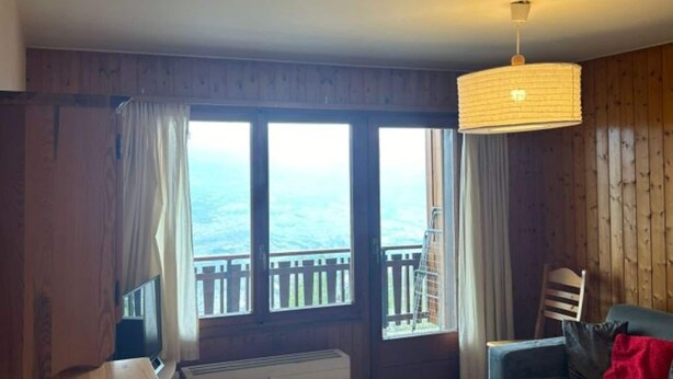Ein Zimmer mit Holzwänden, einem großen Fenster mit Blick und einer Hängeleuchte, sowie einem Sessel.