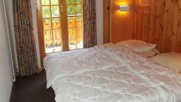 Une chambre avec un grand lit, une fenêtre avec des rideaux et une lampe fixée au mur.