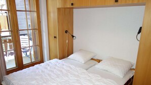 A bedroom with a wooden headboard, a bed with white bedding, and a window with blinds. - Apartment with balcony in Veysonnaz (Les Agettes)