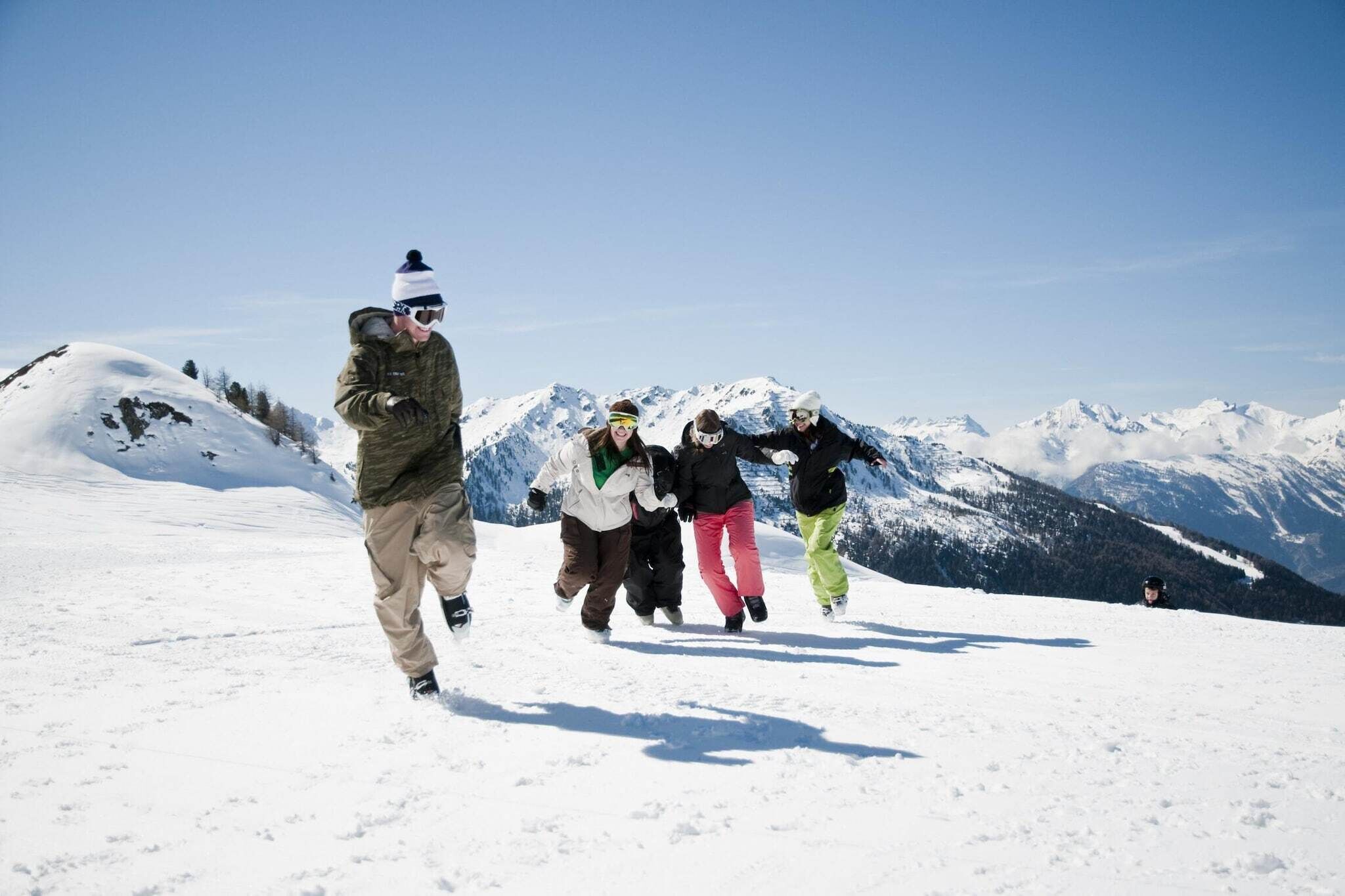 A group of people walking on a snowy mountain with clear skies and snow-covered peaks in the background.