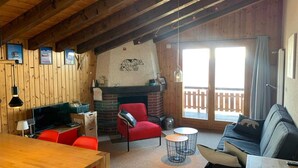 A cozy cabin interior with a wooden ceiling, a fireplace, a TV, a dining area, and a balcony with a wooden railing. - Marvelous apartment with balcony (Les Agettes)