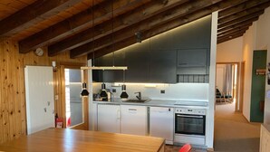 A modern kitchen with stainless steel appliances, wooden ceiling beams, and a dining area with red chairs. - Marvelous apartment with balcony (Les Agettes)