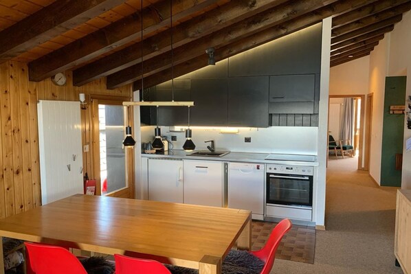 Una cocina moderna con electrodomésticos de acero inoxidable, vigas de techo de madera y un comedor con sillas rojas.