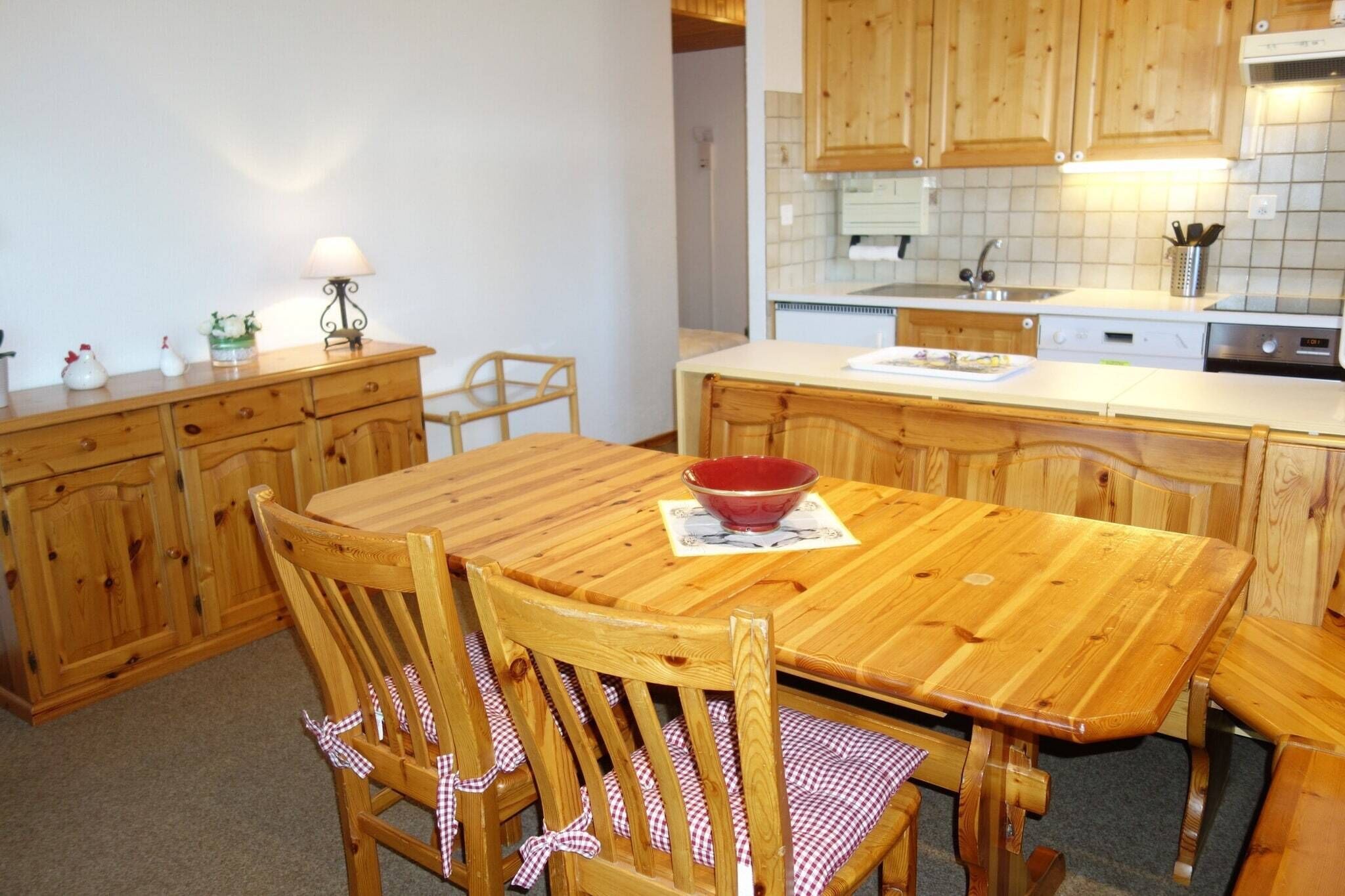 Una mesa de madera con sillas, un tazón rojo y una lámpara sobre un aparador de madera.
