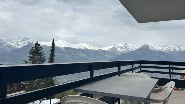 A balcony with a table and chairs overlooking snow-capped mountains. - Charming apartment in Vaysonnaz (Veysonnaz)