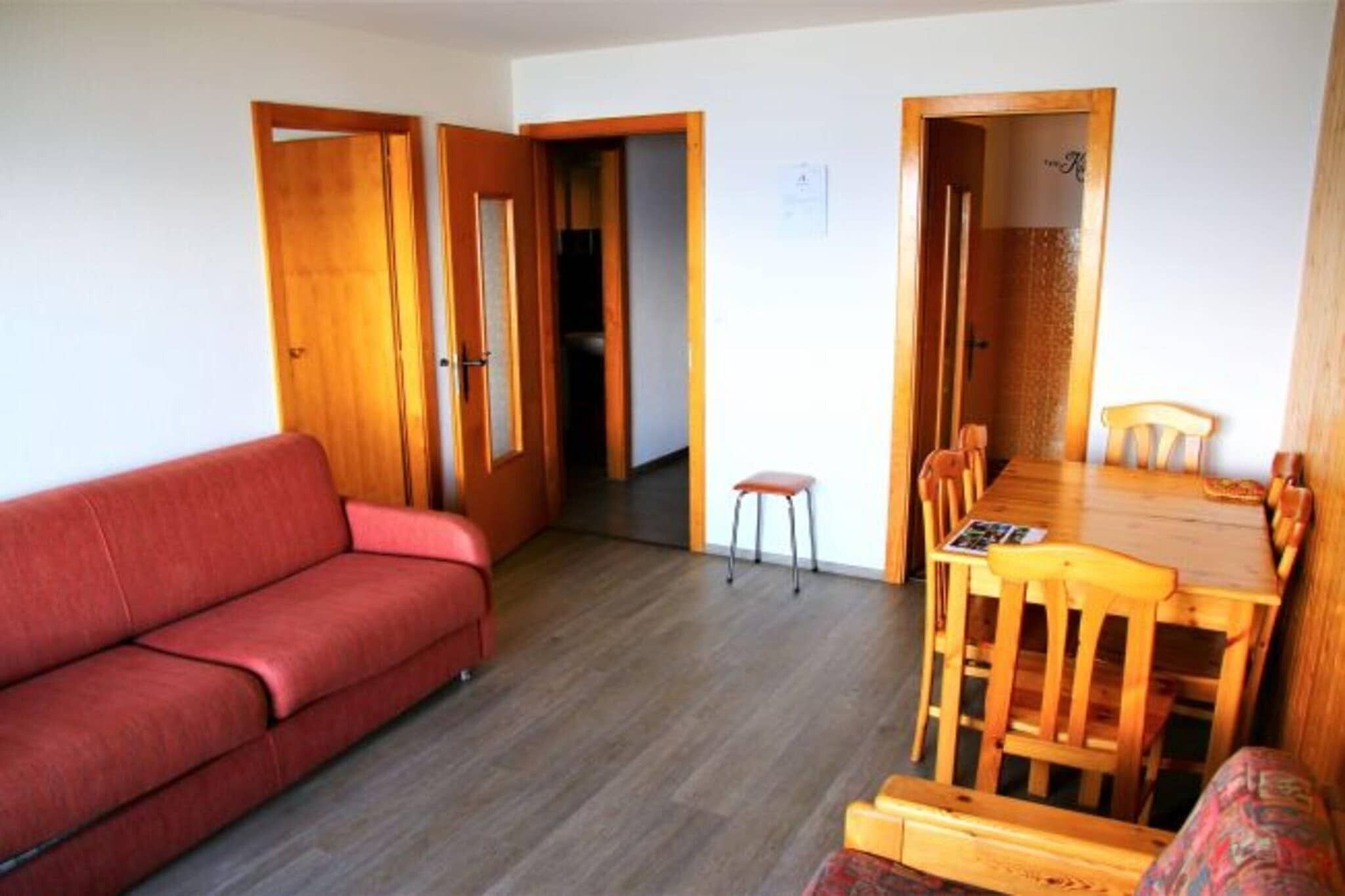 Ein gemütlicher Wohnraum mit einem roten Sofa, einem Holzesstisch mit Stühlen und einem kleinen Hocker.