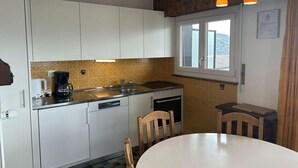 A compact kitchen with white cabinets, a sink, a coffee maker, and a dining area with a table and chairs. - Charming apartment in Vaysonnaz (Veysonnaz)