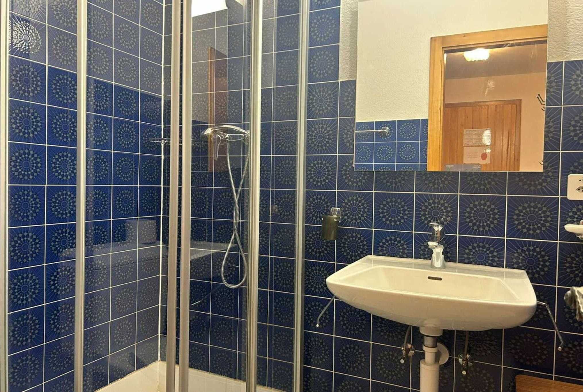 A bathroom with blue patterned tiles, a glass shower enclosure, and a white sink.