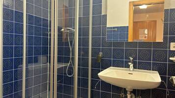 A bathroom with blue patterned tiles, a glass shower enclosure, and a white sink.