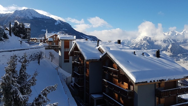 Un resort en la montaña cubierto de nieve, con edificios de madera y una vista despejada de las montañas.