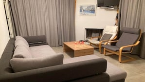 Una sala de estar moderna con un sofá gris, dos sillones, una mesa de centro de madera y una chimenea.