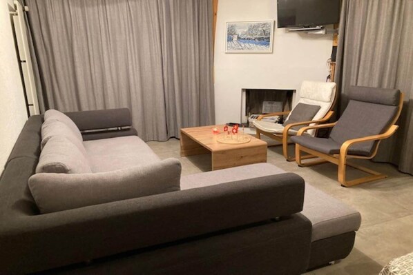 A modern living room with a grey sofa, two armchairs, a wooden coffee table, and a fireplace.