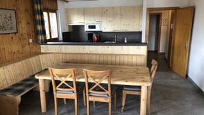Una cocina con armarios de madera, microondas, pileta y comedor con banco y sillas.