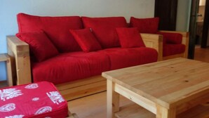 Un canapé rouge agrémenté de plusieurs coussins, une table basse en bois et un pouf à motifs.