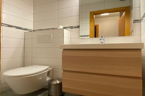 A modern bathroom with a white toilet, a wooden vanity with a mirror, and tiled walls.