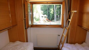 Une petite cabane d’une seule pièce, dotée d’une fenêtre donnant sur une forêt et un terrain de jeux.
