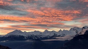 Une chaîne de montagnes aux sommets enneigés, avec un ciel spectaculaire au coucher du soleil.