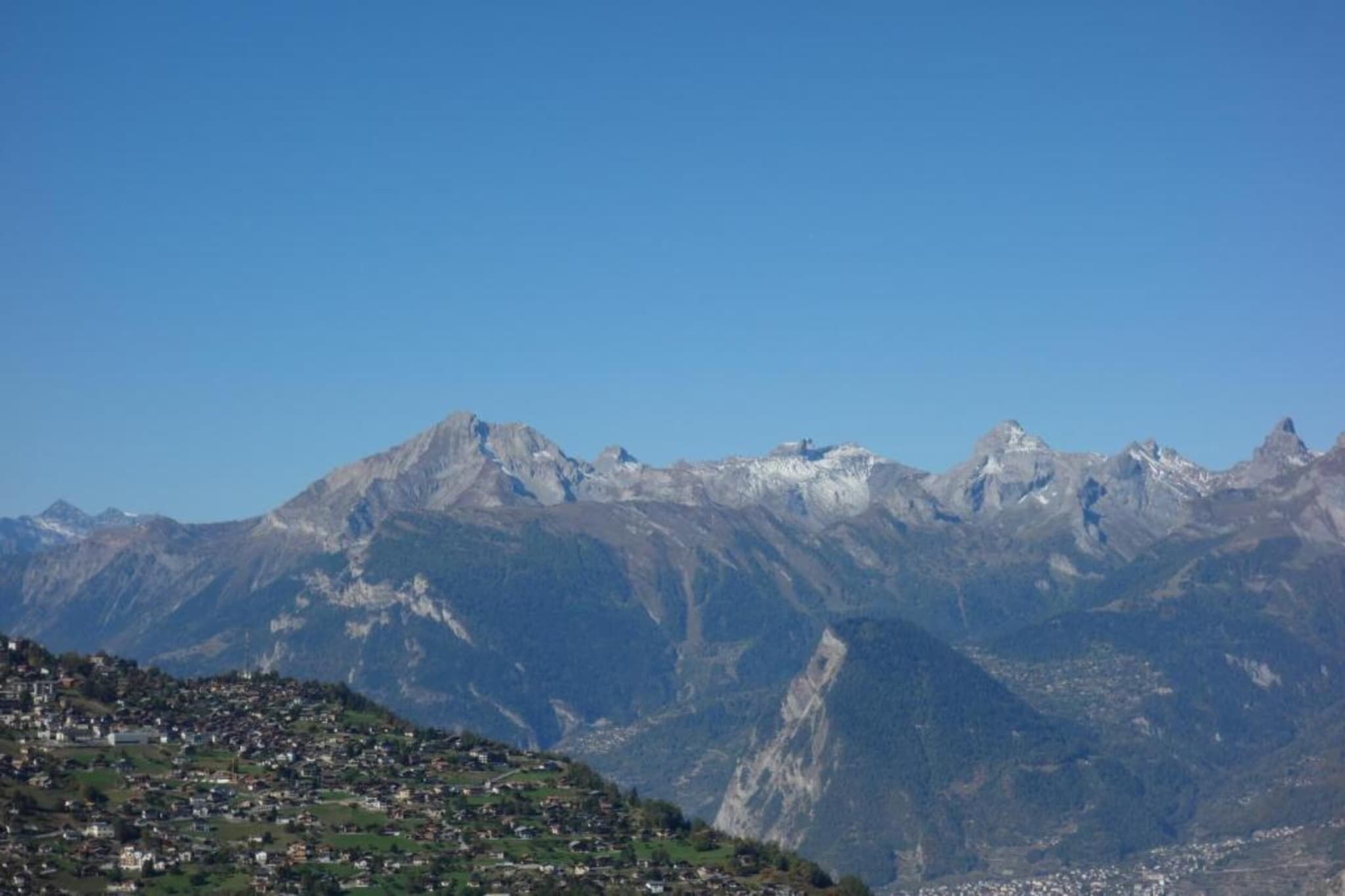 A mountainous landscape with a village in the foreground and snow-capped peaks in the background.