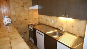 Une cuisine compacte équipée d’un évier, d’une cuisinière et d’un lave-vaisselle, avec des murs carrelés et des meubles en bois.