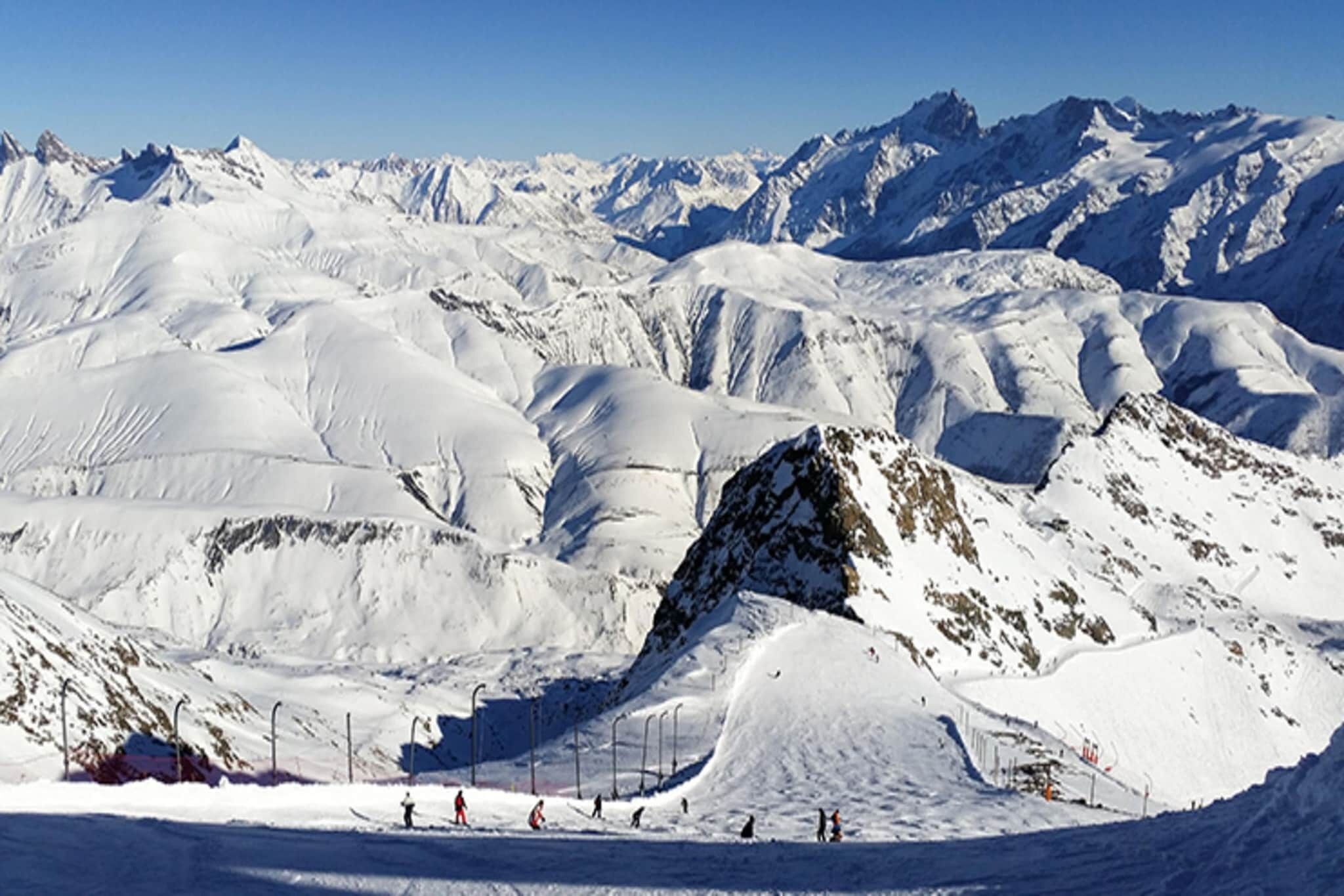 Un paysage montagneux enneigé, avec des pistes de ski et un ciel dégagé.