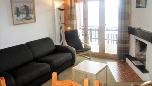 A living room with a black sofa, a wooden chair, a small table, a fireplace, and a balcony with a view. - Apartment near Cable Car with Valley Views (Veysonnaz)
