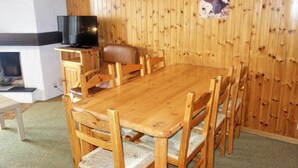 A wooden dining table with six chairs, a television on a wooden stand, and a fireplace. - Apartment near Cable Car with Valley Views (Veysonnaz)